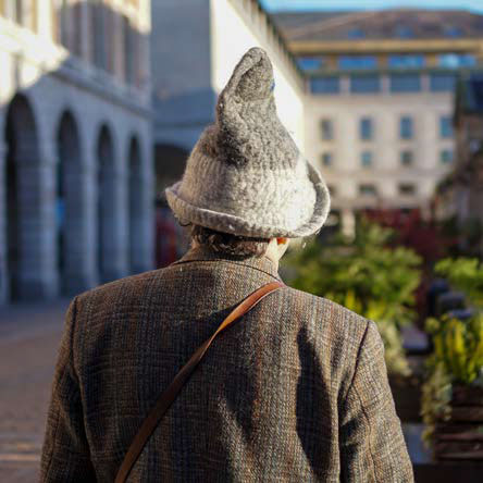 Photo of the back of a man wearing a floppy wizard hat with buildings in front of him