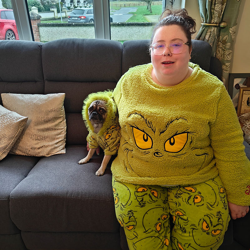 Alison Spittle sat on a sofa with a dog, both wearing Grinch outfits