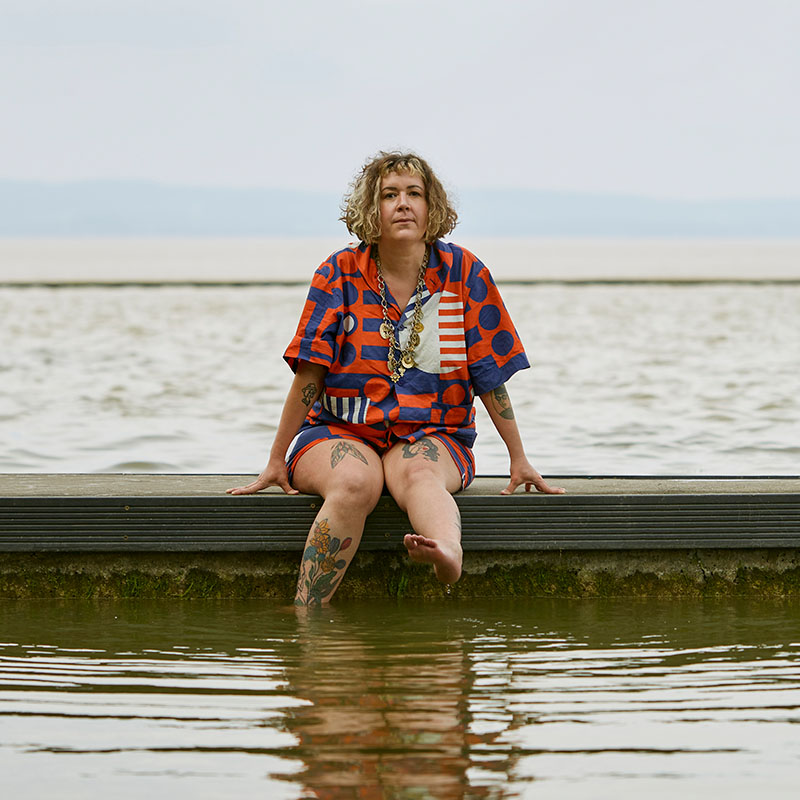 Picture of Amy Mason sat on a sea wall dangling her legs into the water