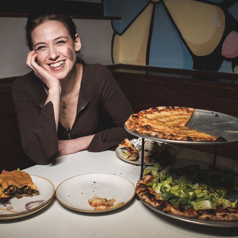 Photo of Chloe Radcliffe smiling at a restaurant table with a double tiered pizza tray in front of her