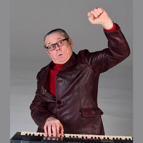 Photo of John Shuttleworth playing the keyboard, making a fist with one arm in air