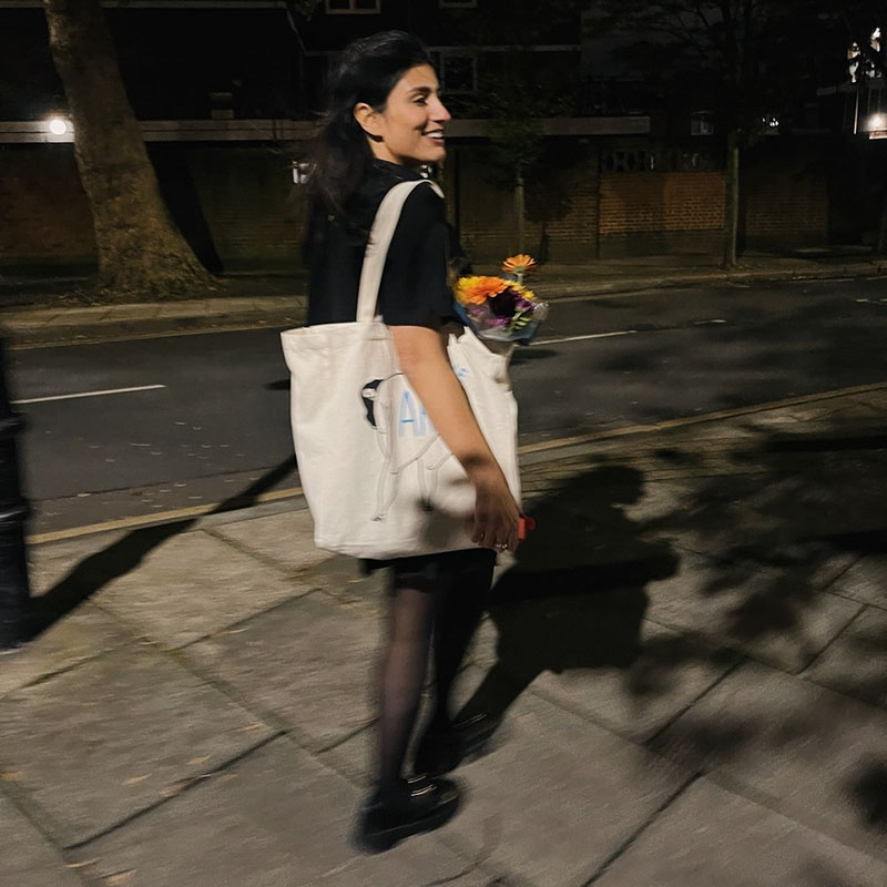 Photo of Celya AB walking along a street at night with a shopping bag over her shoulder