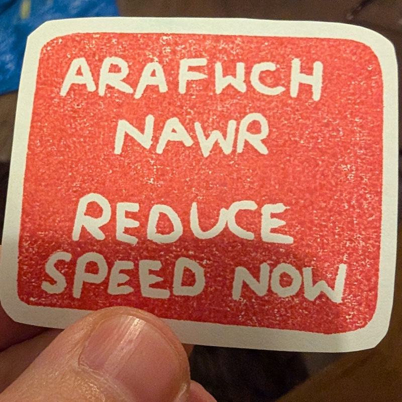 Picture of a hand drawn picture of an 'Arafwch Nawr / Reduce Speed Now' road sign