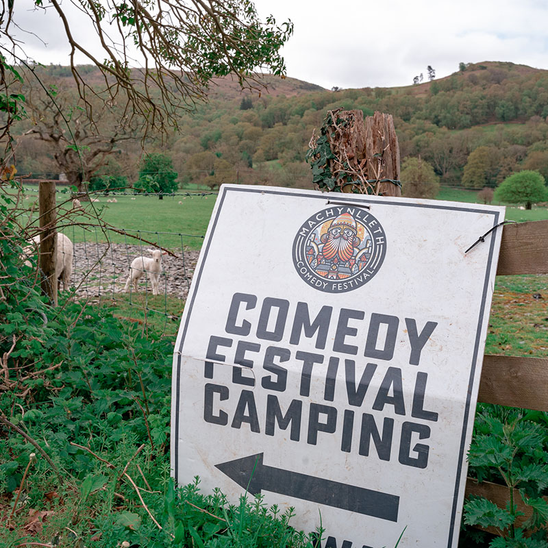 Comedy Festival Camping sign attached to a fence by a field