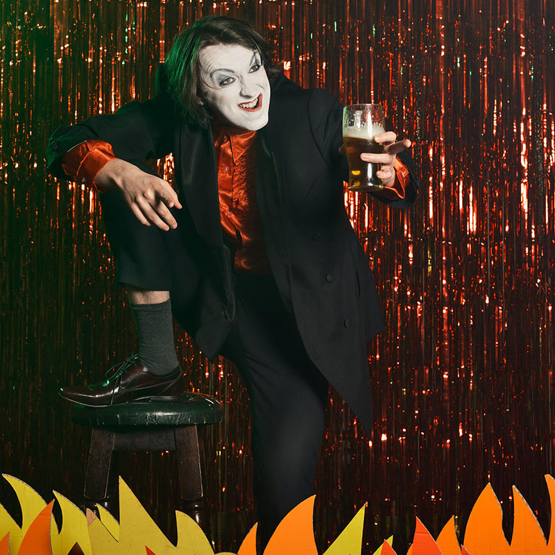 Joe Kent-Walters as Frankie Monroe on stage with a pint in his hand in front of a shiny slash curtain