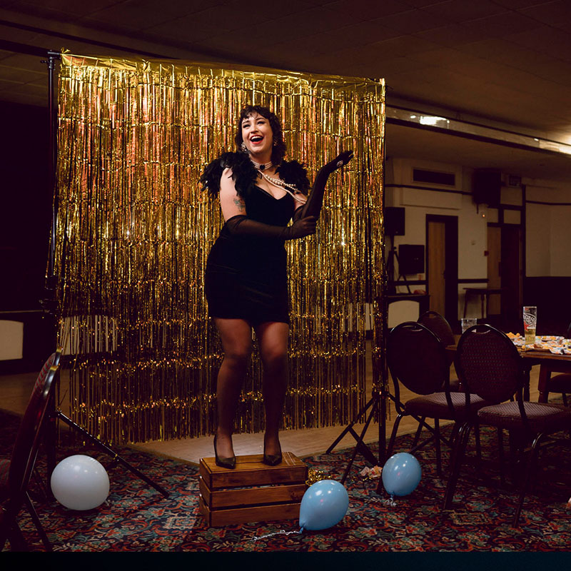 Photo of Molly McGuiness on a makeshift stage in a pub in front of a gold slash curtain