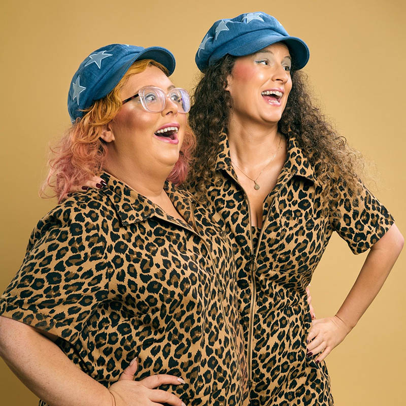 Photo of Alison Spittle and Poppy Hillstead wearing matching leopard print jumpsuits and blue cloth caps