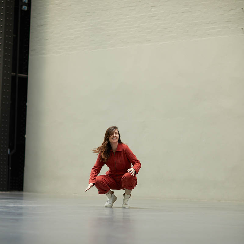 Photo of Madeline squatting down in the middle of a large, empty studio space