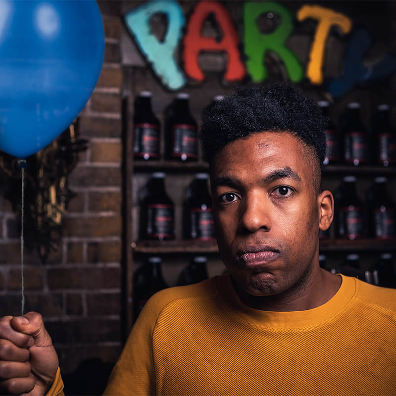 Photo of Toussaint Douglass holding a balloon with other balloons in the background spelling PARTY