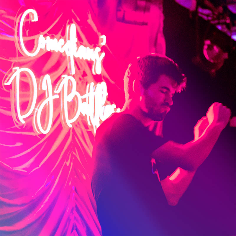 Photo of Ivo Graham dancing in front of a Comedians' DJ Battles neon sign