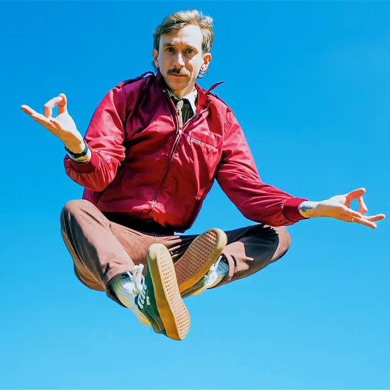 Photo of Rob Copland in mid-air doing and 'ohm' pose against a bright blue sky