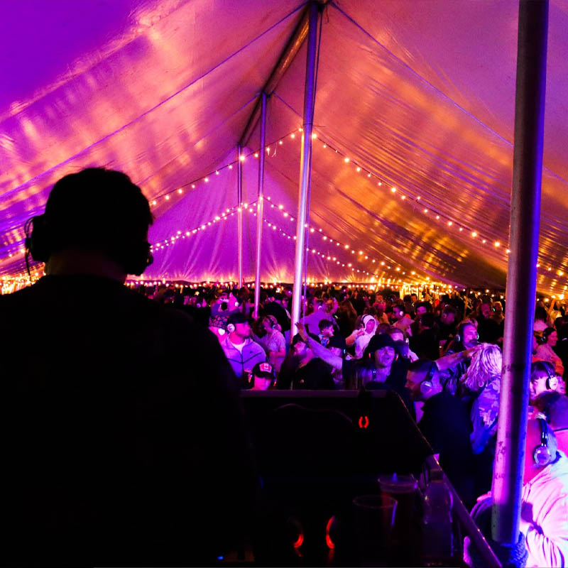 Photo of a DJ on stage playing to a crowd who are all wearing headphones in a marquee