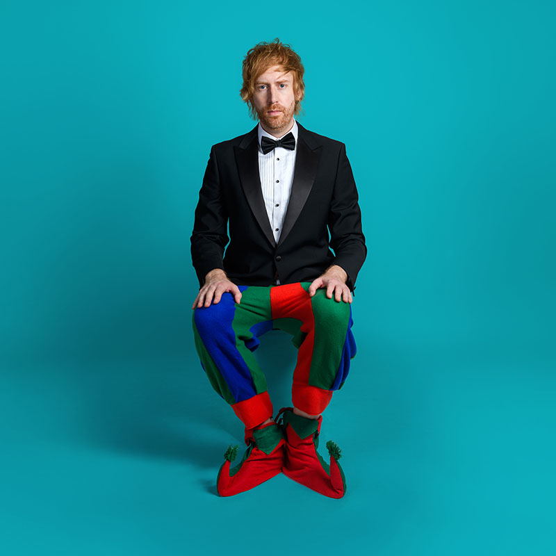 Picture of Mark Simmons wearing a tuxedo jacket and bow tie with checkered jester's trousers and shoes