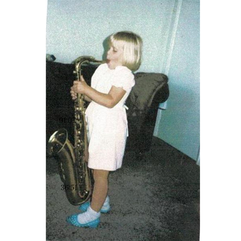Photo of Sara as young child playing the saxaphone in a house