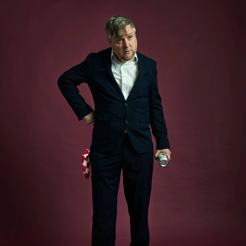 Photo of Tim Key in a suit holding a can of lager
