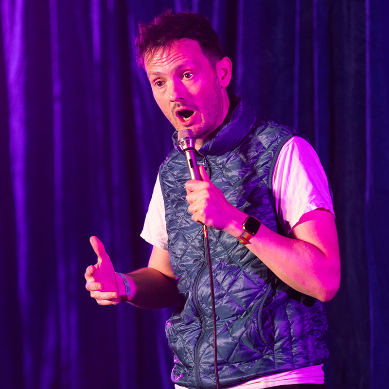 Photo of Stuart Laws on stage with a mic in hand and wearing a blue gilet