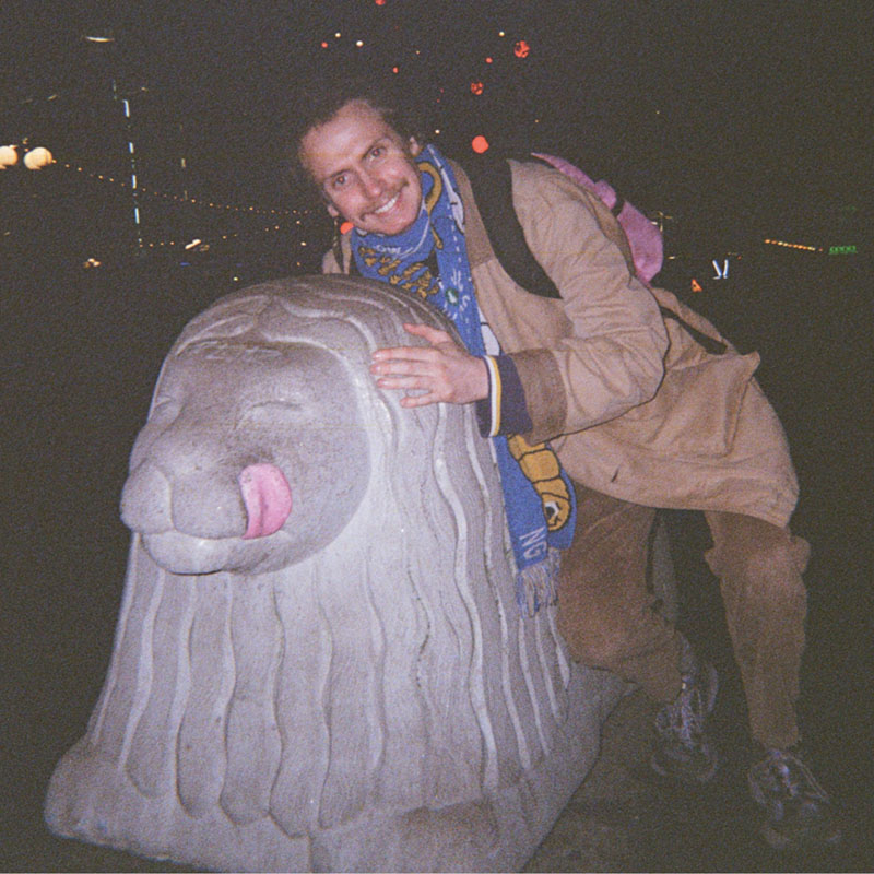 Photo of Mikey posing next to a large stone statue of a lion