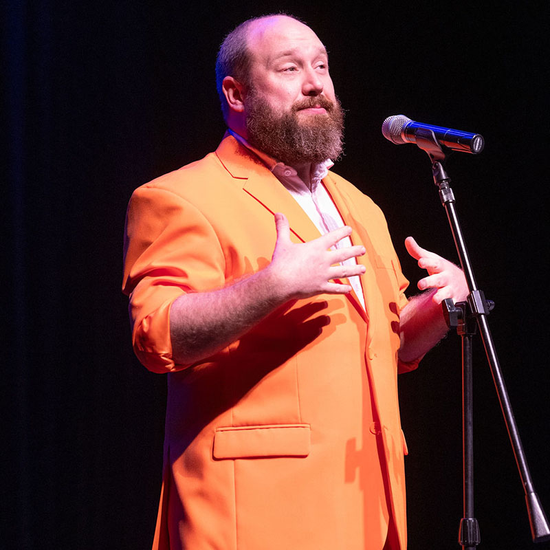 Photo of Jonny Donahoe in front of a mic wearing an orange suit