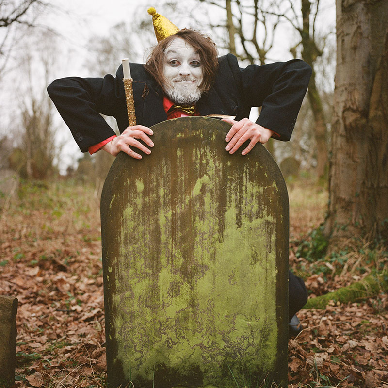 Photo of Frankie Monroe popping up from behind a headstone in a graveyard wearing a party hat