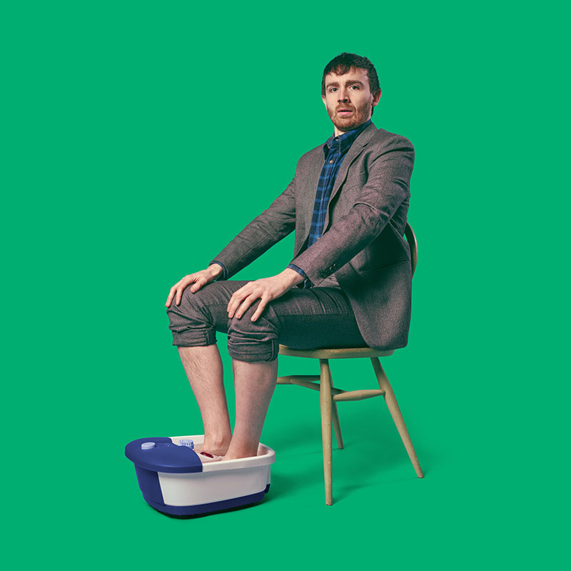 Photo of Ian Smith sat in a chair with trousers rolled up and both feet in a foot spa