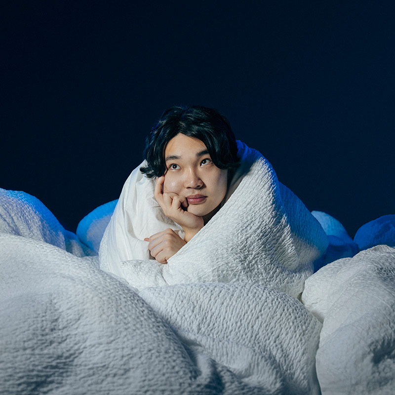 Photo of Li Jin Hao wrapped up in a white duvet with just his head popping out, resting on his hand