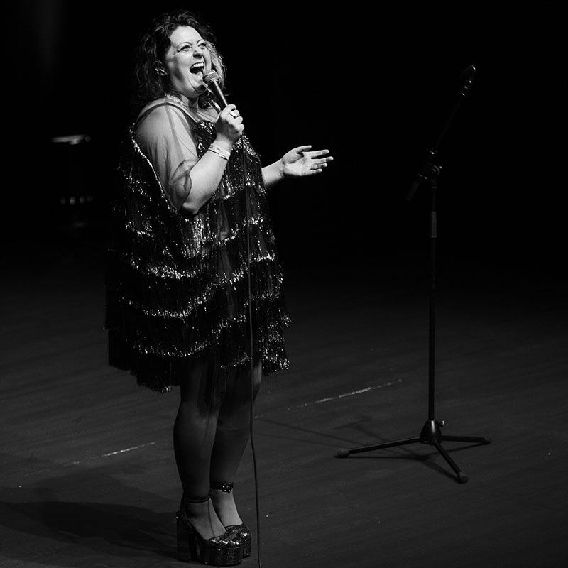 Black & White photo of Kiri Pritchard-McLean on stage in Aberystwyth hosting the 2025 showcase