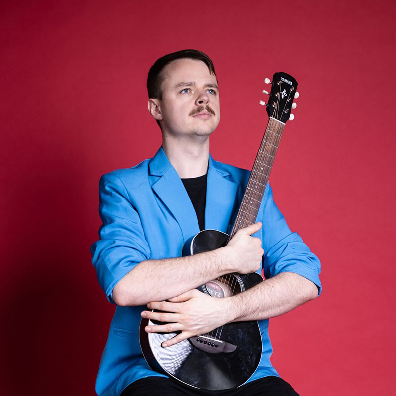 Photo of David Hoare clutching his guitar