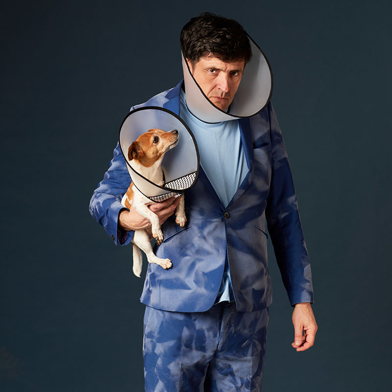 Photo of Spencer Jones holding a dog under his arm. Both have cone collars around their neck.