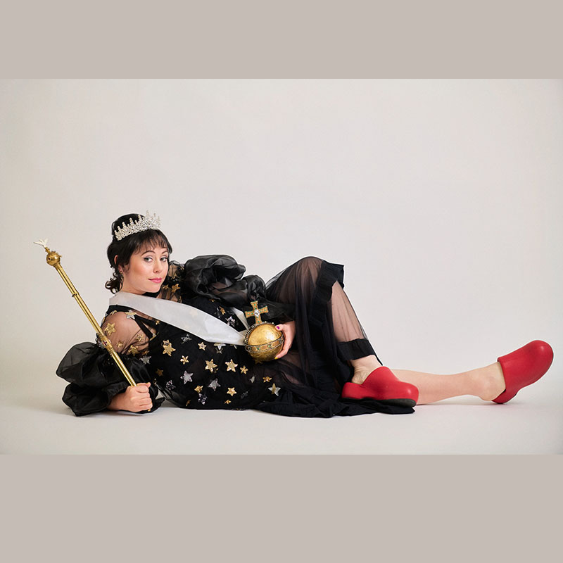 Picture of Amy Annette lying down. She has a sash around her, a tiara on her head and is holding an orb and sceptre