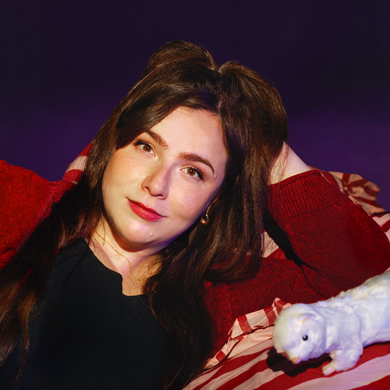 Photo of Anna Thomas lying down with a small, stuffed toy ferret next to her