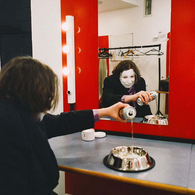 Photo of Frankie Monroe in a dressing room. You can see him in the mirror and he's pouring a can of lager into a dog bowl