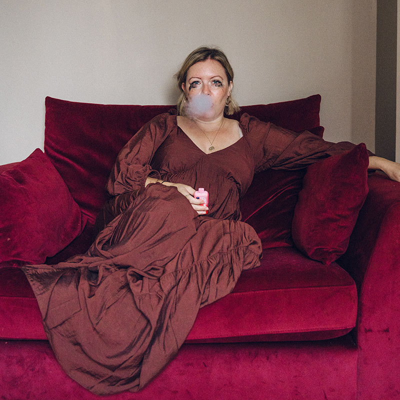 Picture of Katie Gill-Williams sat on a sofa with mascara running down her face, exhaling vape smoke